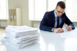 Stack of documents on the desk and male employee working on background